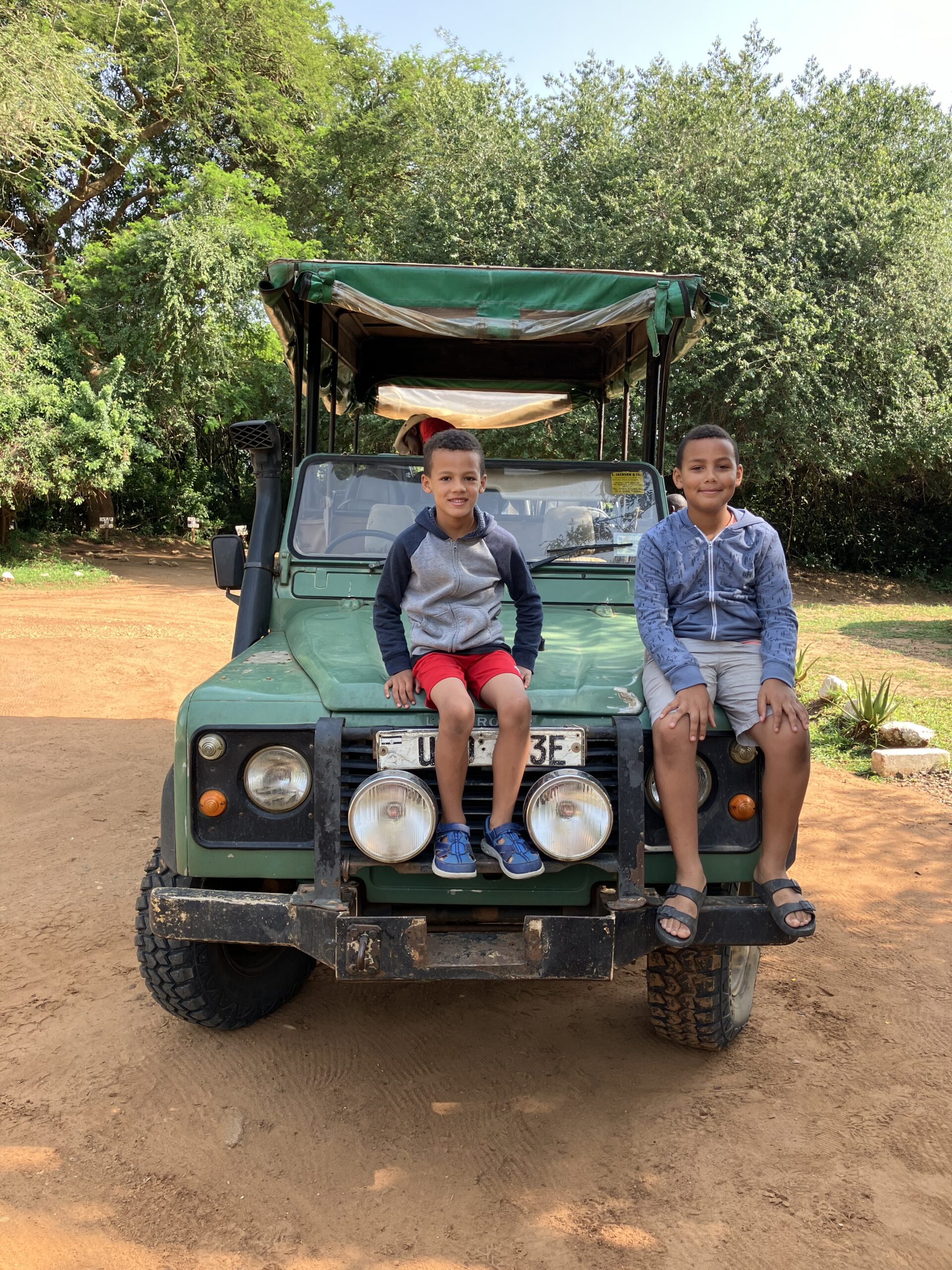 Two boys sitting on the hood of a safari vehicle waiting for their next adventure in Uganda
