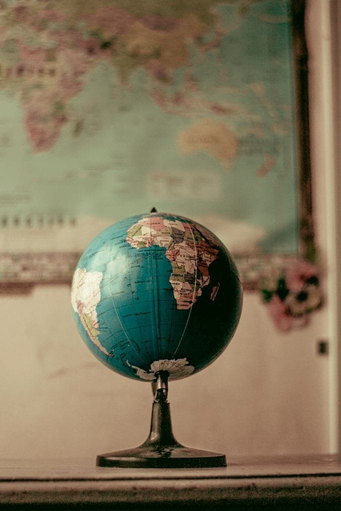 A globe positioned on a desk with a world map in the background, symbolizing education and global learning.