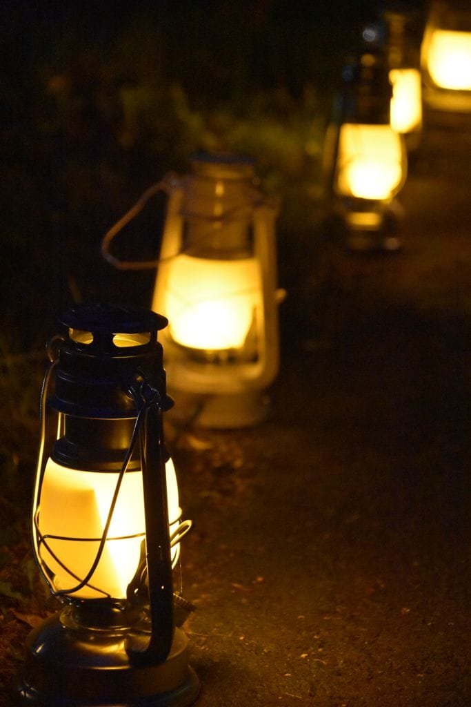 A series of glowing vintage lanterns line a shadowy outdoor pathway.