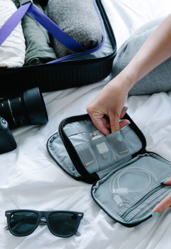 Close-up view of travel essentials including sunglasses and electronics organizer on a bed.