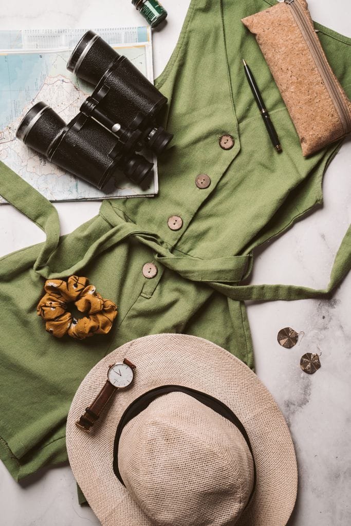 Flat lay of a travel outfit with binoculars, hat, and map for an adventure theme.