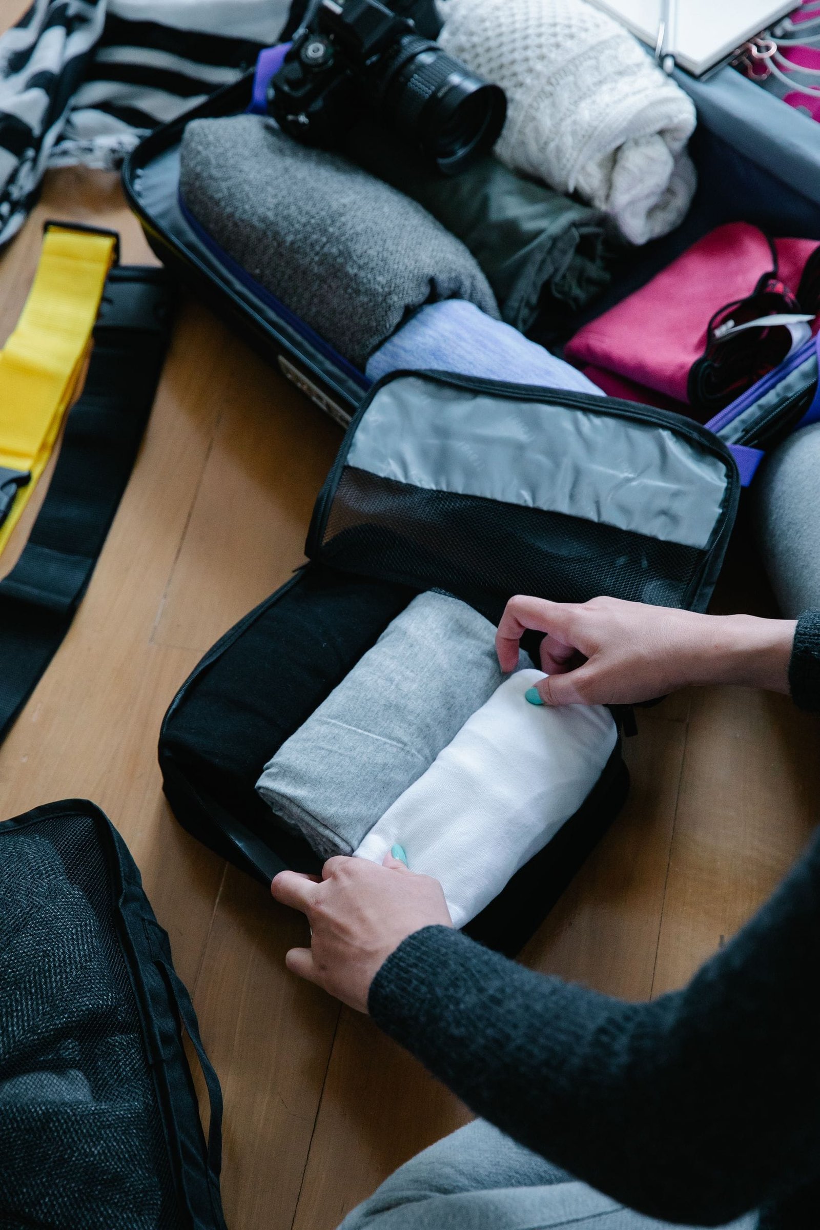 Hands folding clothes into a packing cube with a DSLR camera nearby for travel.